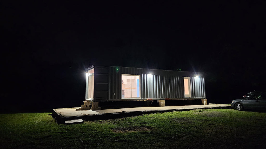 A Utopia shipping container home at night with its windows lit from inside
